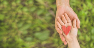 A parent and child holding a red heart in their hands. Representing how child therapy in Katy, TX can improve child-parent relationships. Call us today to begin child counseling.