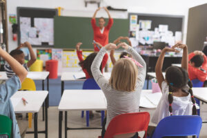 A group of kids holding their arms in a circle in a classroom. With our child counseling in Katy, TX, your child can learn stress management skills. Call us today to learn more!