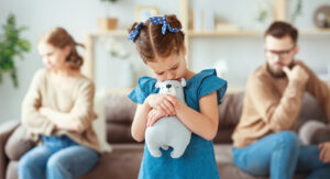 A family sitting on a couch while a little girl hugs a stuffed animal in the middle. Representing how child therapy in Katy, TX can help with divorce transitions. To learn more, call us today!