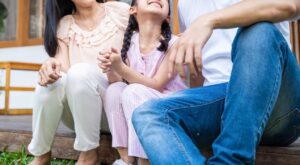 A family all smiling & sitting together on a porch. Our child counseling for anxiety in Katy, TX can help your child thrive. Call us today to get started. 