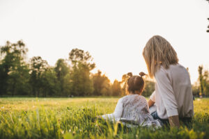 A mother & daughter sitting down in a grassy field. Our therapy for children in Katy, TX can help with divorce, custody & more. Learn more by calling us today.