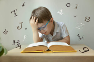 A young boy resting his head on his hand while he reads a book. If your child is reluctant to go to school because of anxiety, call us today to begin child therapy. We offer child therapy for anxiety in Katy, TX. 