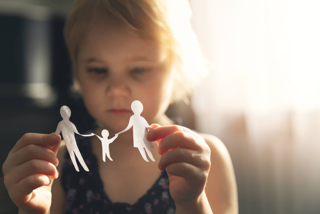 A young child holding a paper cutout of a family. Representing how child counseling in Katy, TX can help children thrive through divorce. Start your child's healing journey today.