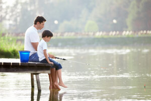 A father & son fishing at a river while sitting on the dock. Child counseling for children of divorce can help them thrive despite the changes. Call us today to get started with a child therapist in Katy, TX.