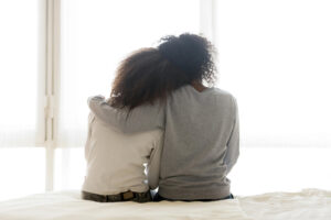 A mother hugging her teen daughter while sitting down on a bed. Representing the signs that parents need to watch out for with at-risk teens. Our teen counseling in Katy, TX can help you & your child thrive. 