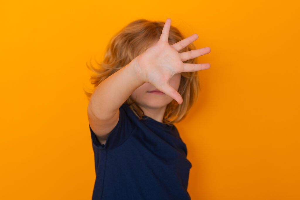 Child making stop gesture in front of orange background. Representing how children with anxiety may struggle to do things alone. If this sounds like your child, call us to begin child counseling for anxiety in Katy, TX.