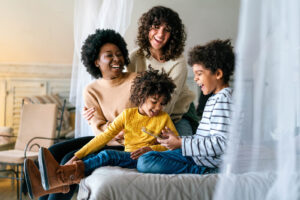 A family sitting on a bed together all laughing & smiling. Our child counseling in Katy, TX can help your family and child thrive. Call today to get started with a child therapist. 