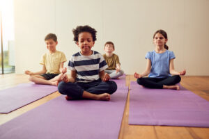 A group of children sitting in yoga poses on the ground. Representing how mindfulness for children can help with emotional dysregulation. Reach out today to begin child counseling in Katy, TX. 