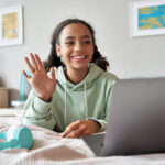 A teen girl waving at her laptop & smiling. Representing how online therapy for teens in Katy, TX can help your child with at-risk behaviors. Call today to begin!