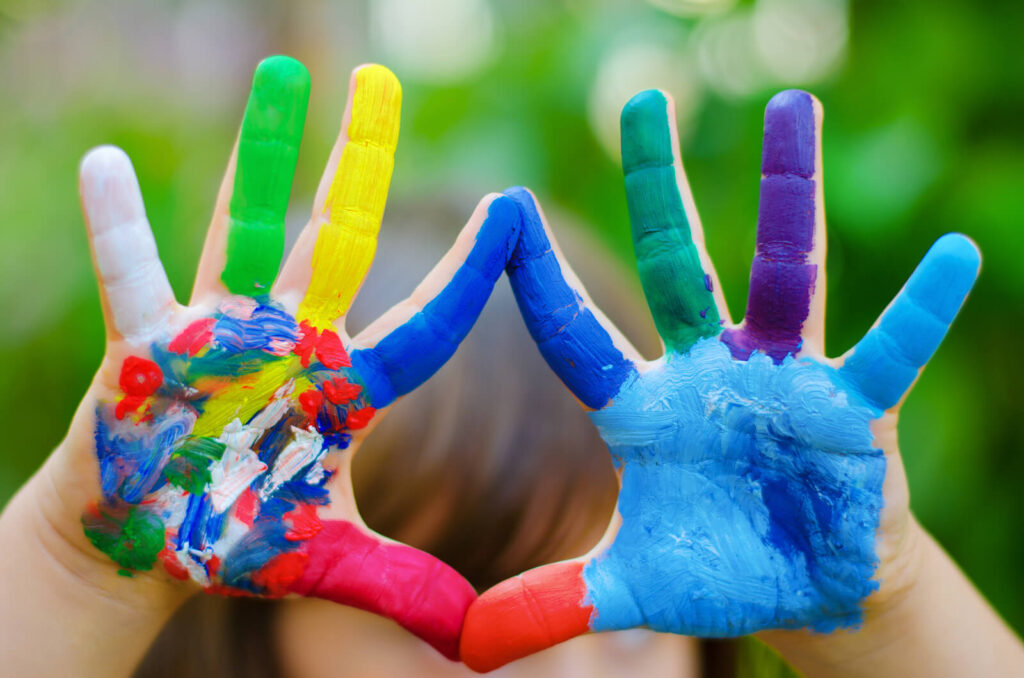 A close-up of a young child's hands painted in rainbow colors. Our child therapy in Katy, TX & LENS Neurofeedback can help with anxiety & more. 