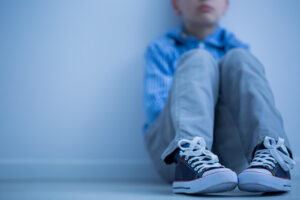 A young boy sitting alone on the ground. Representing anxiety in children & how it can feel isolating. Get started with a child therapist in Katy, TX today!