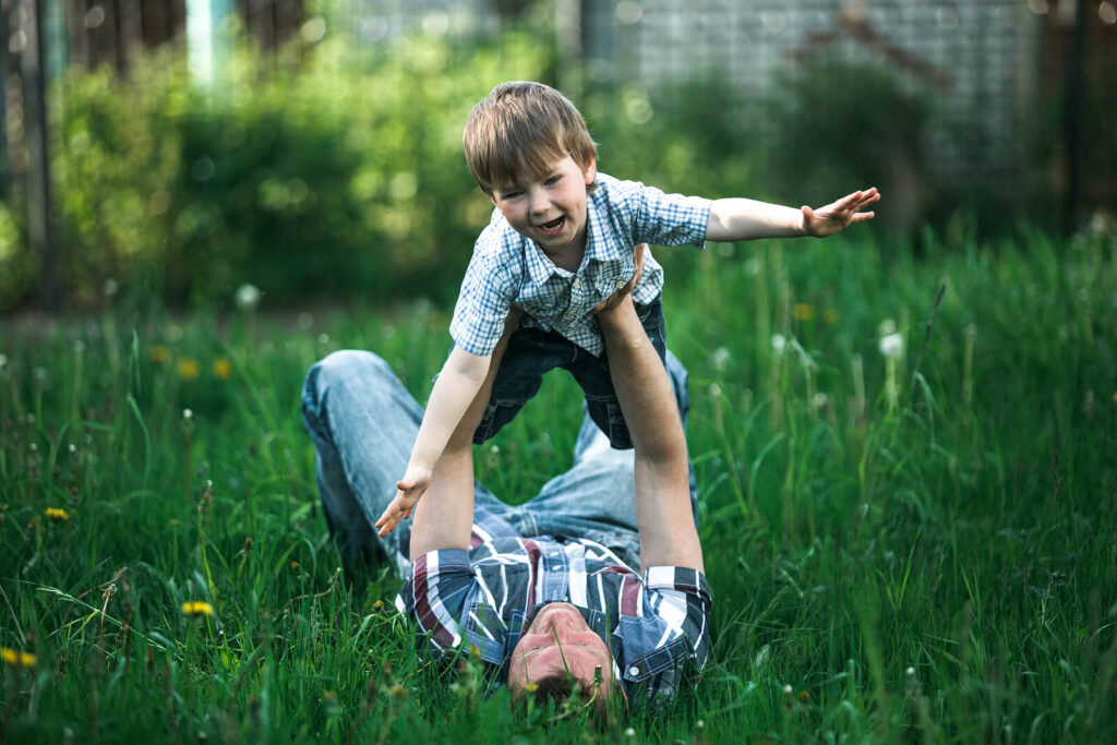 A father holding their son in the air playing airplane. Read our blog here to discover how child counseling in Katy, TX & LENS neurofeedback can help with anxiety. Call today to begin!