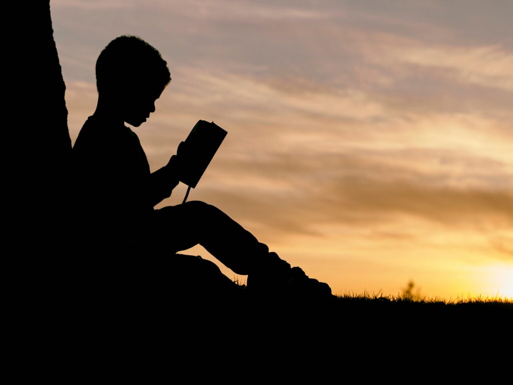 An silhouette of a young boy reading a book in an open area. To leran more about how our child behavioral therapy in Katy, TX, reach out to us today. We can help your family thrive.