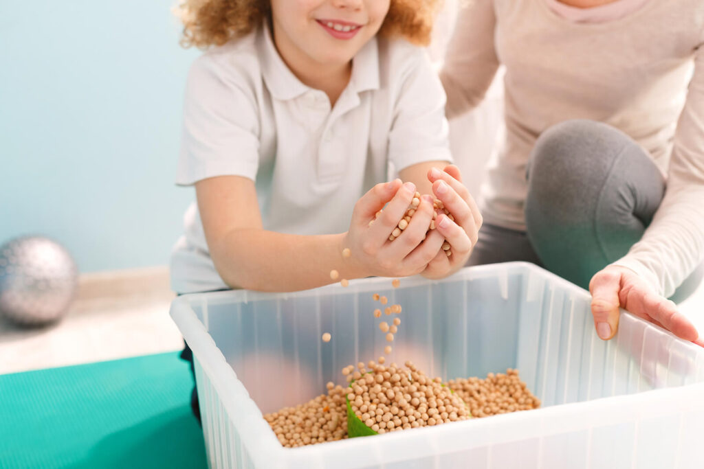 A child playing with chickpeas in a container while sitting next to a child therapist. Representing how our approach at WHCC is compassionate in helping children understand their anxiety. Get started with child anxiety counseling in Katy, TX today.