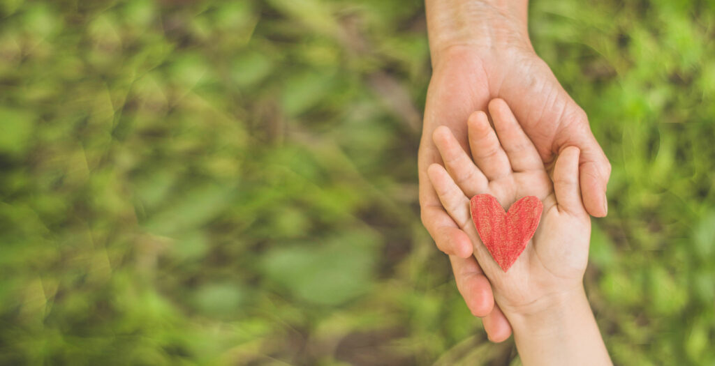 An adult hand holding a child's hand who is resting a red heart in their palm. Read our blog here for more information on child behavioral therapy in Katy, TX. We can help your child thrive!