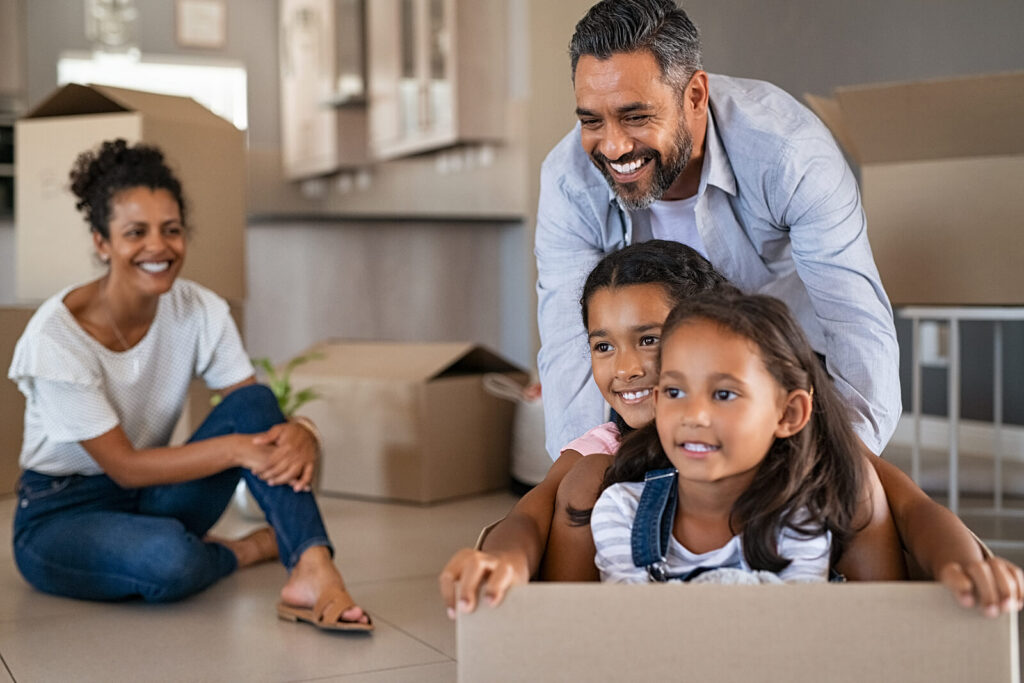 A father pushing his daughters in a large moving box in the living room while the mom watches. This represents how our therapy for children in Katy, TX can help with life transitions & anxiety. Reach out today to begin!