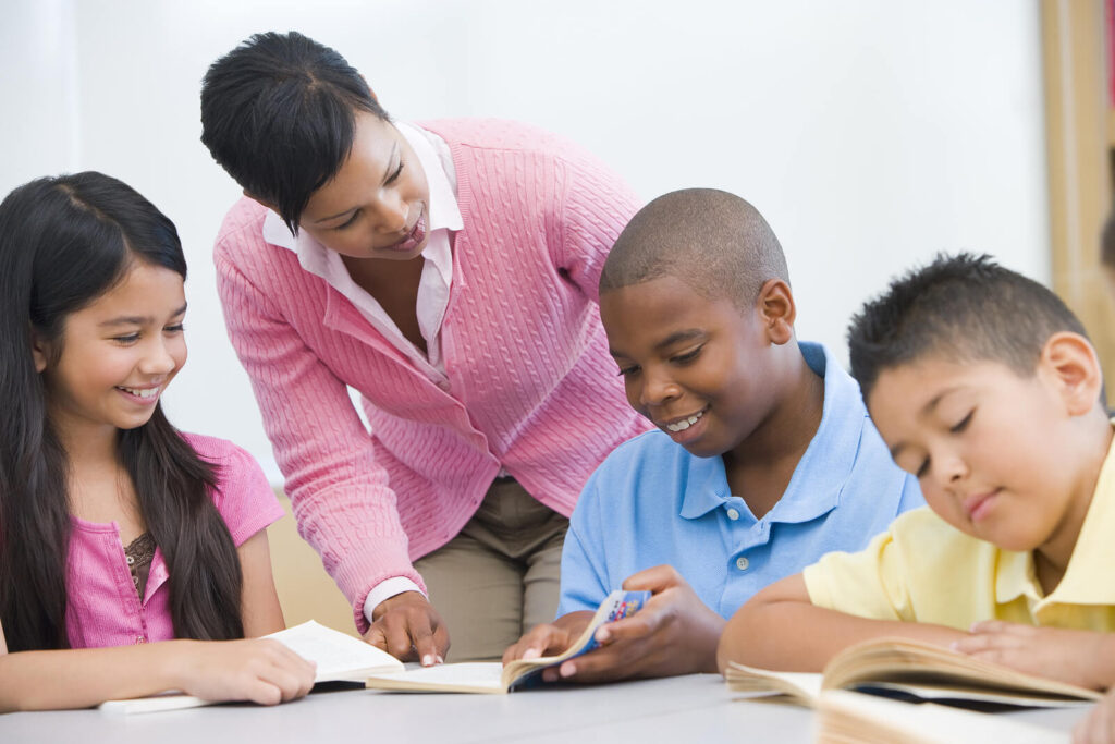 A group of diverse students talking to a teacher while smiling & reading. Our child anxiety counseling in Katy, TX is here to empower kids & families. Reach out today to get started. 