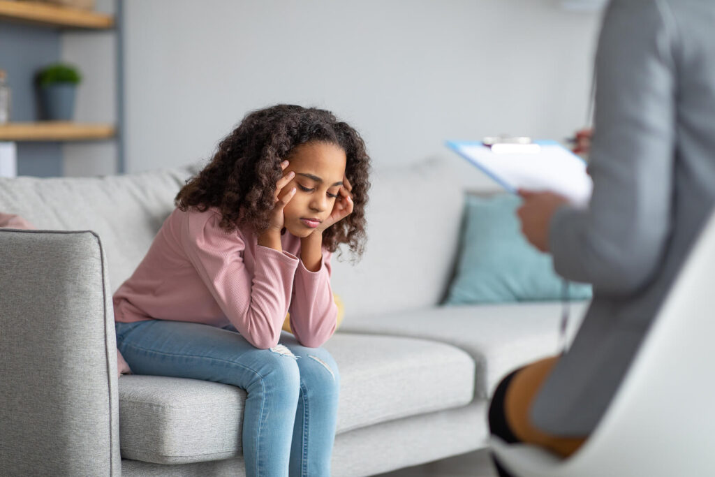 A child holding their head wearing a pink shirt sitting in child therapy. Our child behavioral therapy in Katy, TX can help parents understand their behaviors better. Get started with a child therapist today!