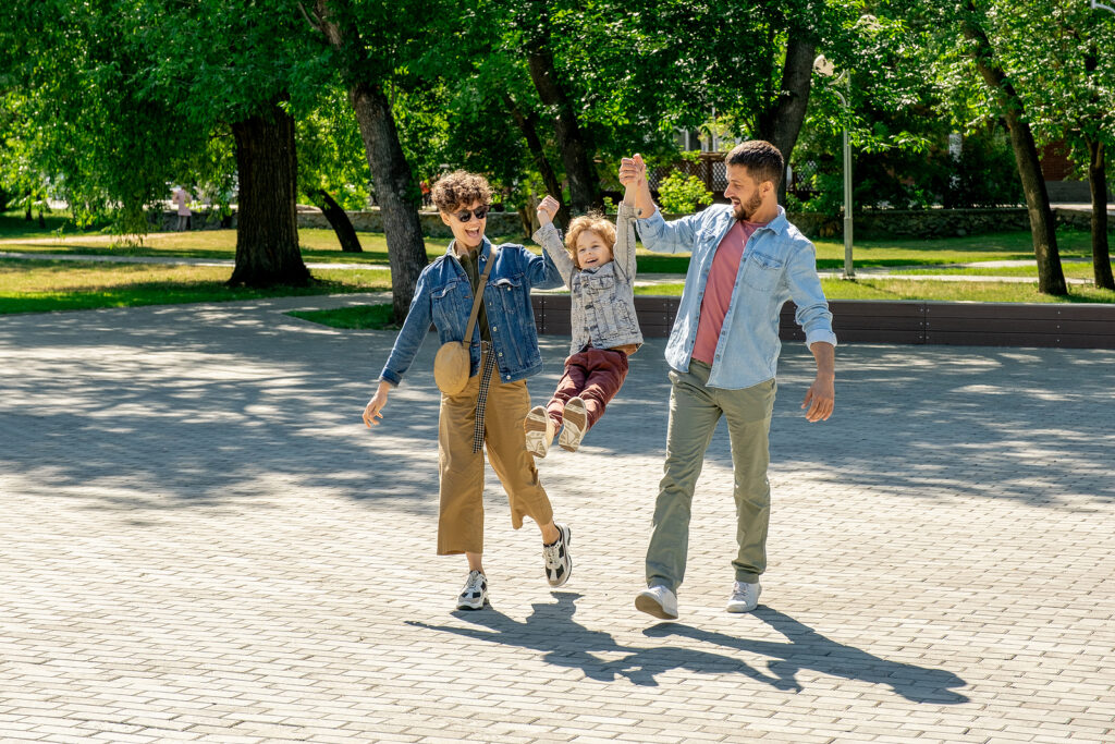 Two parents swinging their child in the air while walking through a park. Representing how our child therapy in Katy, TX can help with behavioral challenges, communication between children & more. Read our blog for more info! 