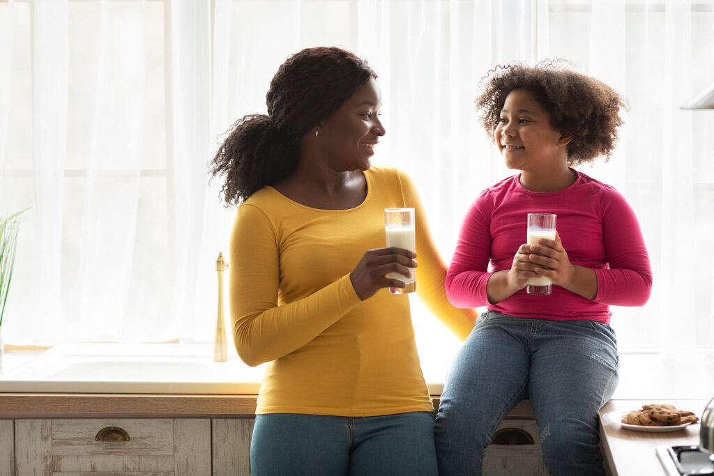 A daughter sitting on the counter drinking milk with her mom smiling. Child therapy in Katy, TX can help your child navigate big emotions. Call us today to start their healing journey.