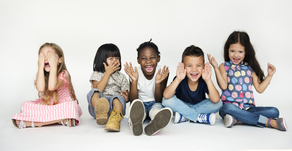 A group of diverse children sitting down showing happy & joyful faces. This represents how emotional regulation in children can be challenging. With the support of a child behavioral therapist in Katy, TX, your child can build resilience. 