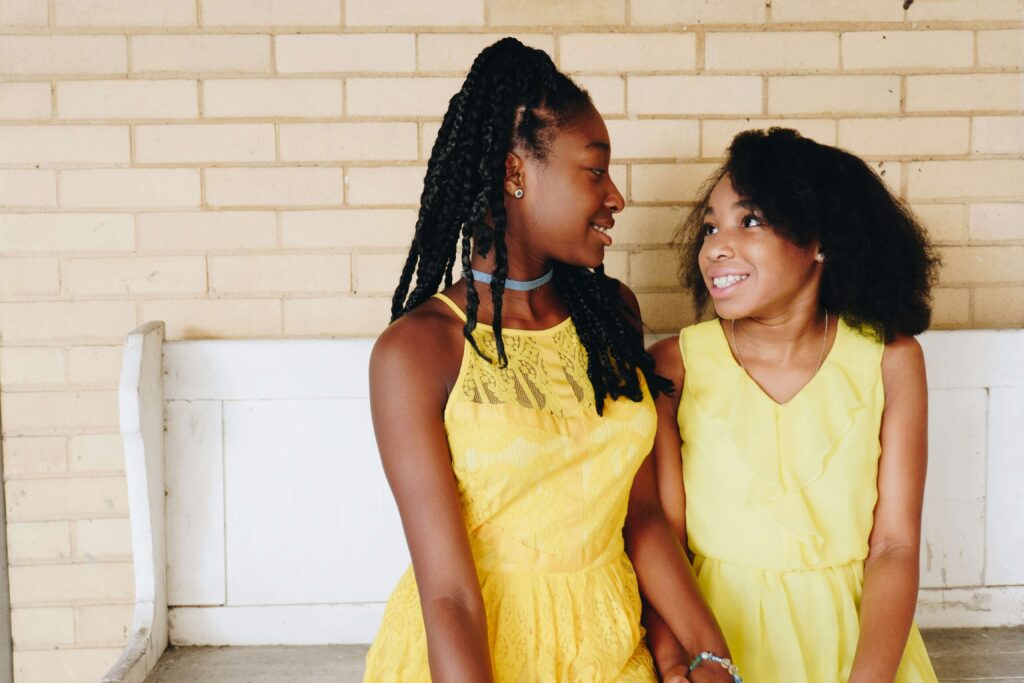 Two young black girls sitting on a bench wearing pretty yellow dresses. Is your teen struggling with anxiety? Our teen counseling in Katy, TX can help!