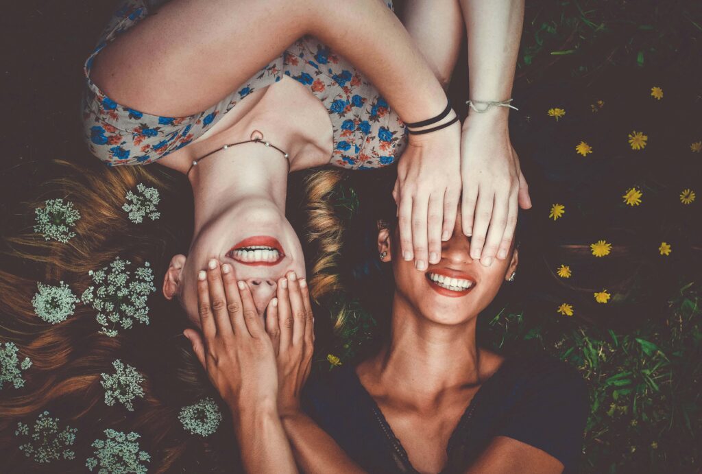 Two teen girls laying on the ground covering each other eyes with their hands with flowers in their hair. Teen counseling in Katy, TX can help your teen manage anxiety, stress & more. Get started today!