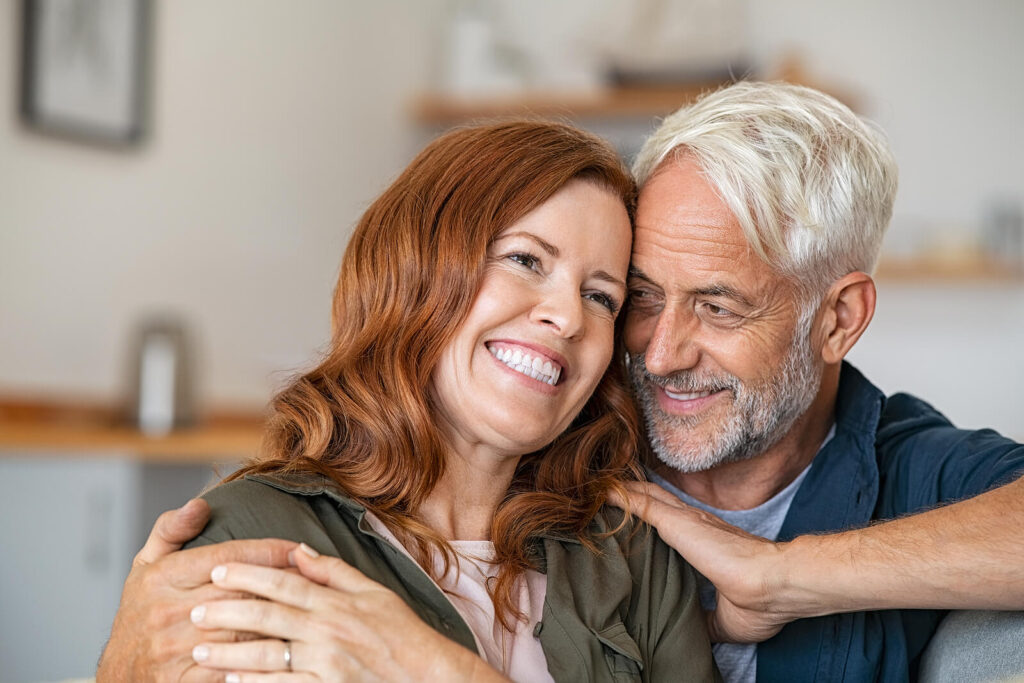 An older couple smiling together & sitting closely on a couch. If you want to work on your communication & build a stronger relationship, couples therapy in Katy, TX can help. Reach out today to get started!