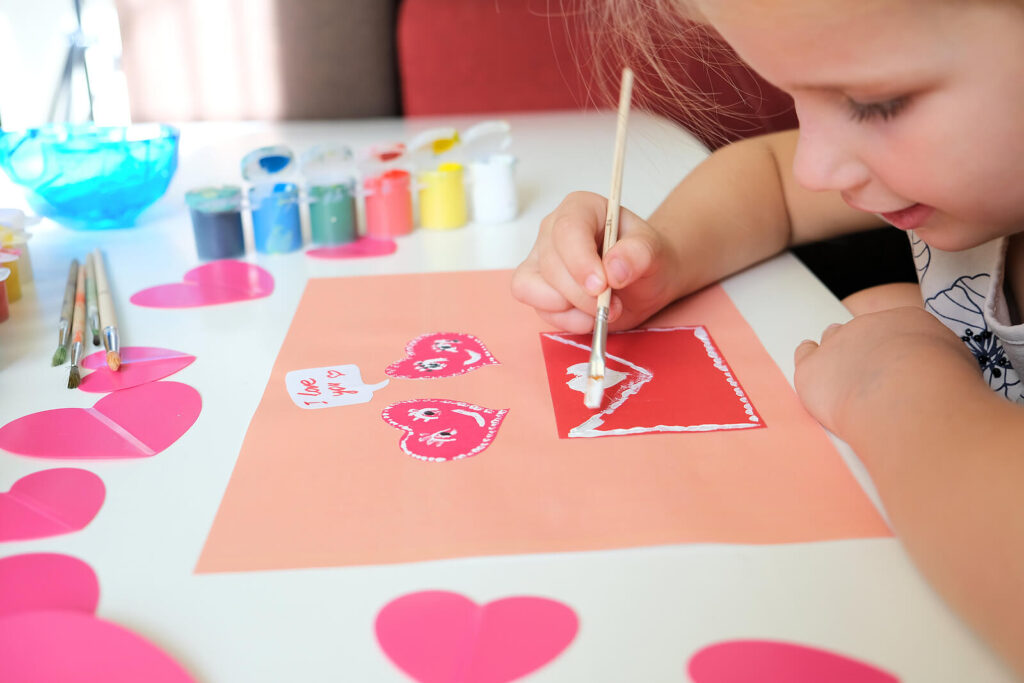 A young girl doing a Valentine's Day craft on a pink piece of paper. Valentine's Day is a great opportunity to show your child they are deserving of love & respect. Learn how child counseling in Katy, TX can help them build positive friendships. 