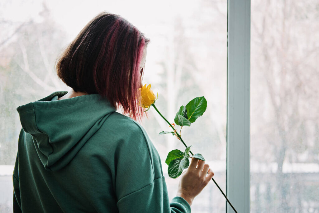 A young teen girl with pink highlights smelling a yellow rose in front of a window. If you want your child to get out of a toxic friendships, consider reaching out to a child therapist in Katy, TX. They can support your children's friendships.