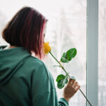 A young teen girl with pink highlights smelling a yellow rose in front of a window. If you want your child to get out of a toxic friendships, consider reaching out to a child therapist in Katy, TX. They can support your children's friendships.