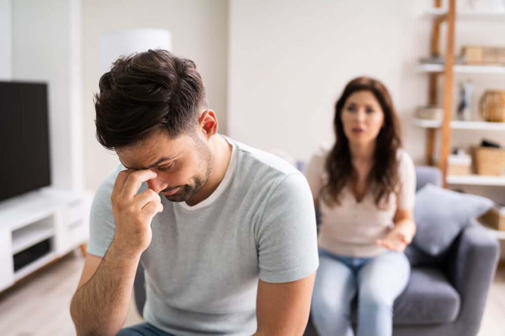 A man turning away from his talking partner while grabbing the bridge of his nose. Representing how it feels when a partner refuses therapy. Couples therapy in Katy, TX can help your connection!