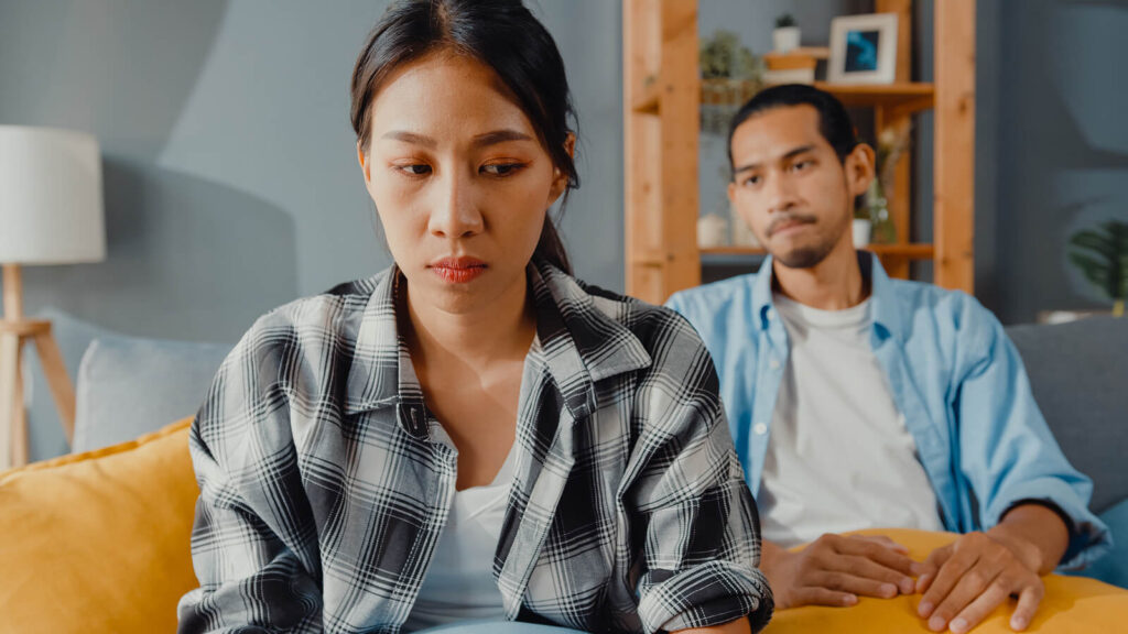 A woman sitting away from her partner on the couch looking upset. If your husband refuses to go to therapy, reach out to WHCC today. We offer couples therapy in Katy, TX & individual counseling.