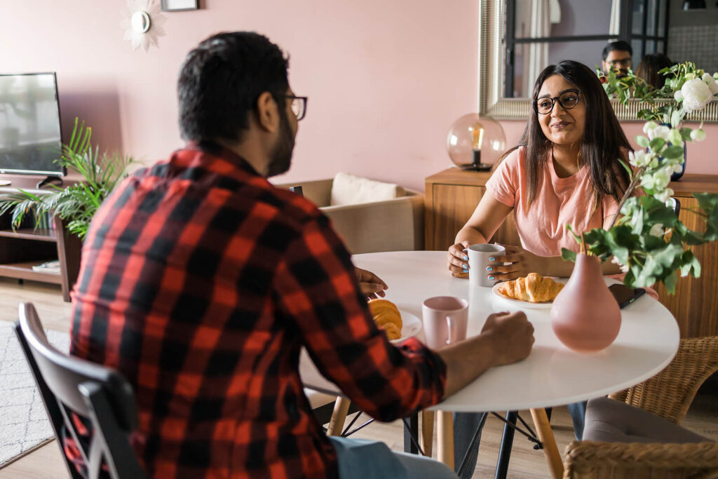 A diverse couple sitting down at a cafe table while having a conversation. This represents how important communication is in relationships. To learn more, get started with couples therapy in Katy, TX. 