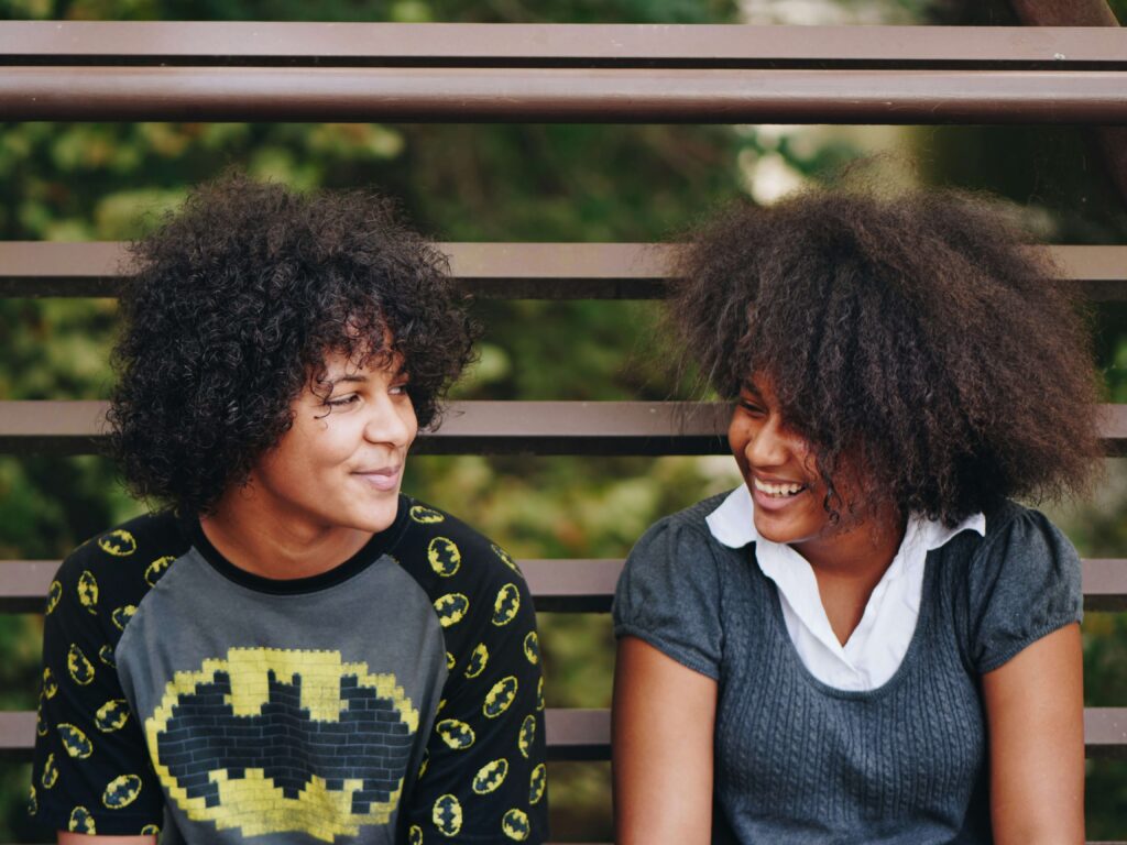 Two teenagers sitting on school bleachers laughing with each other. Child therapy in Katy, TX can help your kids build positive friendships. Call us today to get started.