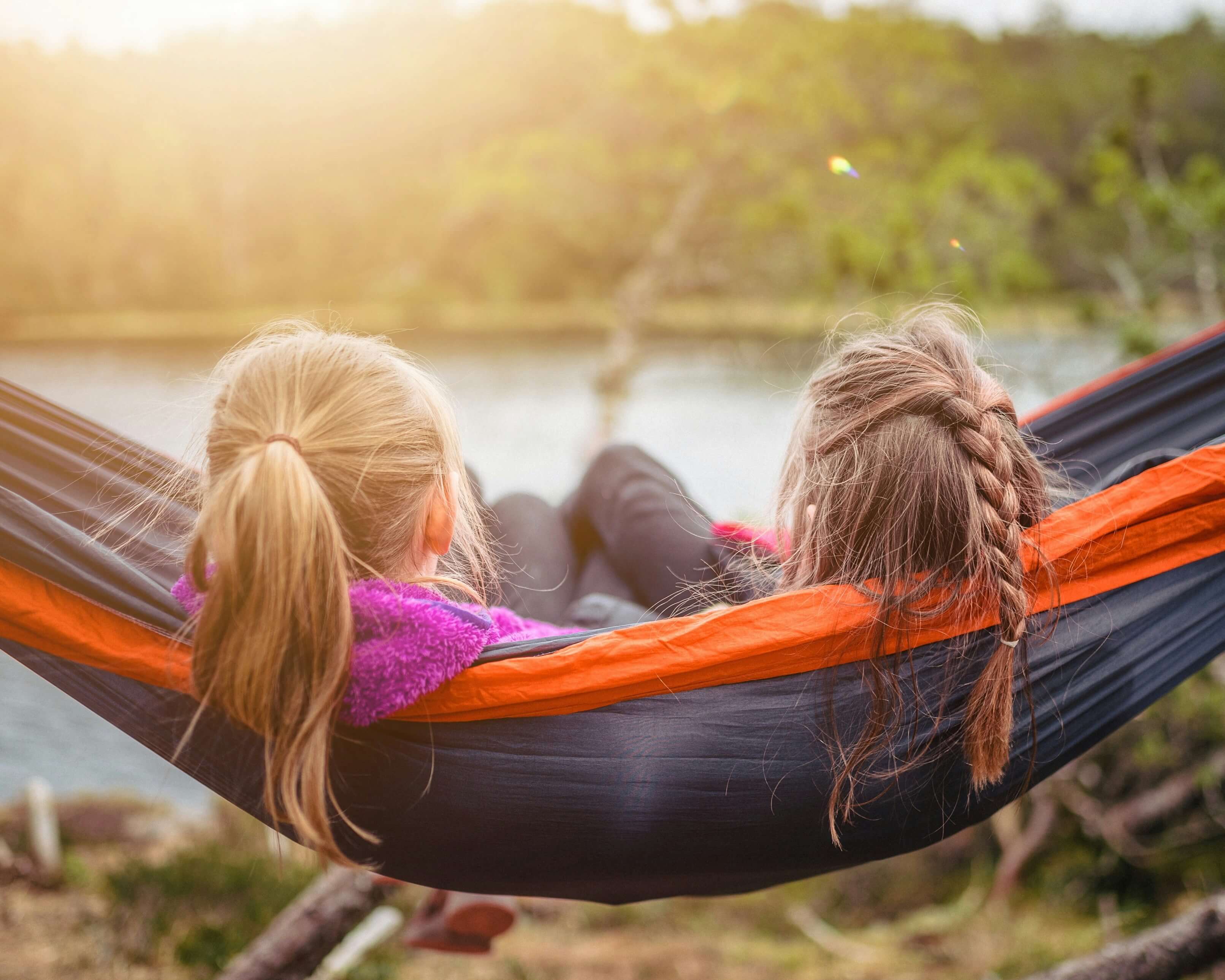 Two young girls sitting together in a hammock near the water. Representing how child counseling in Katy, TX can help your child build resilient friendships. Reach out today to get started.