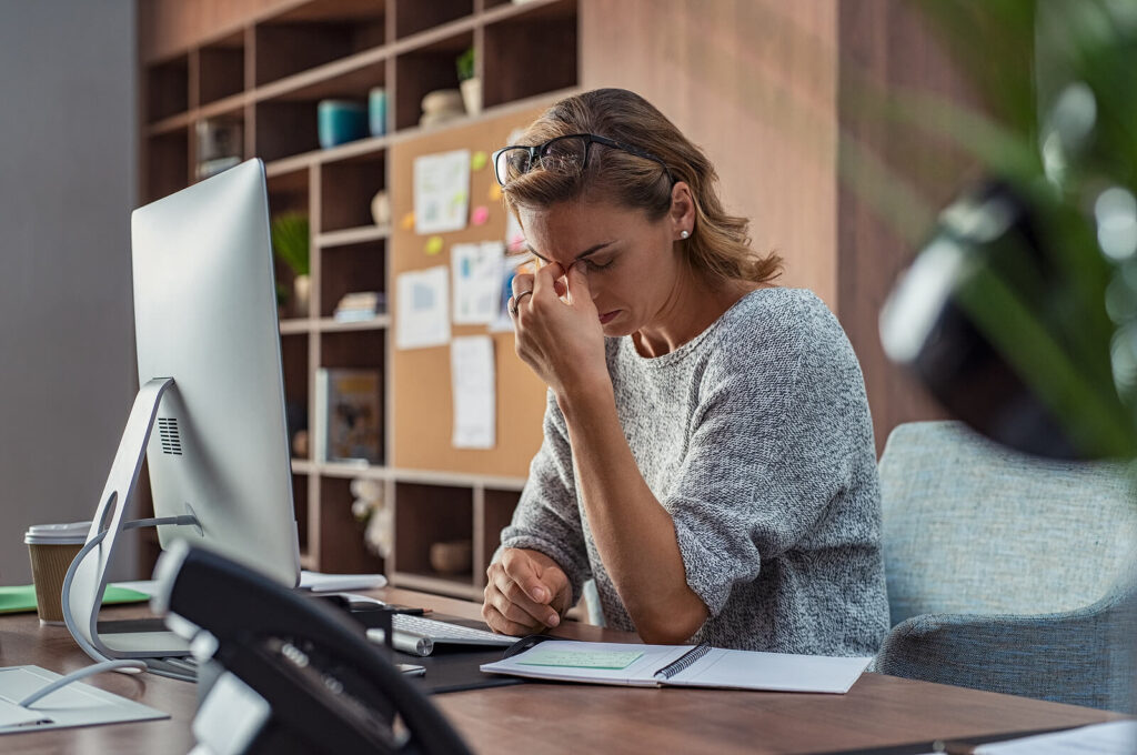 stressed businesswoman | counseling katy | therapy katy | therapy near me | katy, texas | houston, tx | Texas A stressed business woman pinching the bridge of her nose at her desk. Therapy in Katy, TX can help with stress & anxiety. Develop healthy coping mechanisms today!