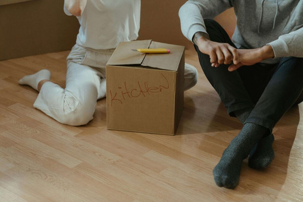 moving boxes | counseling katy | therapy katy | therapy near me | katy, texas | houston, tx | Texas Two individuals sitting near a packed moving box labeled "Kitchen". Representing how therapy in Katy, TX can help with life transitions such as moving, a new job or a loss. Reach out today for personalized support.