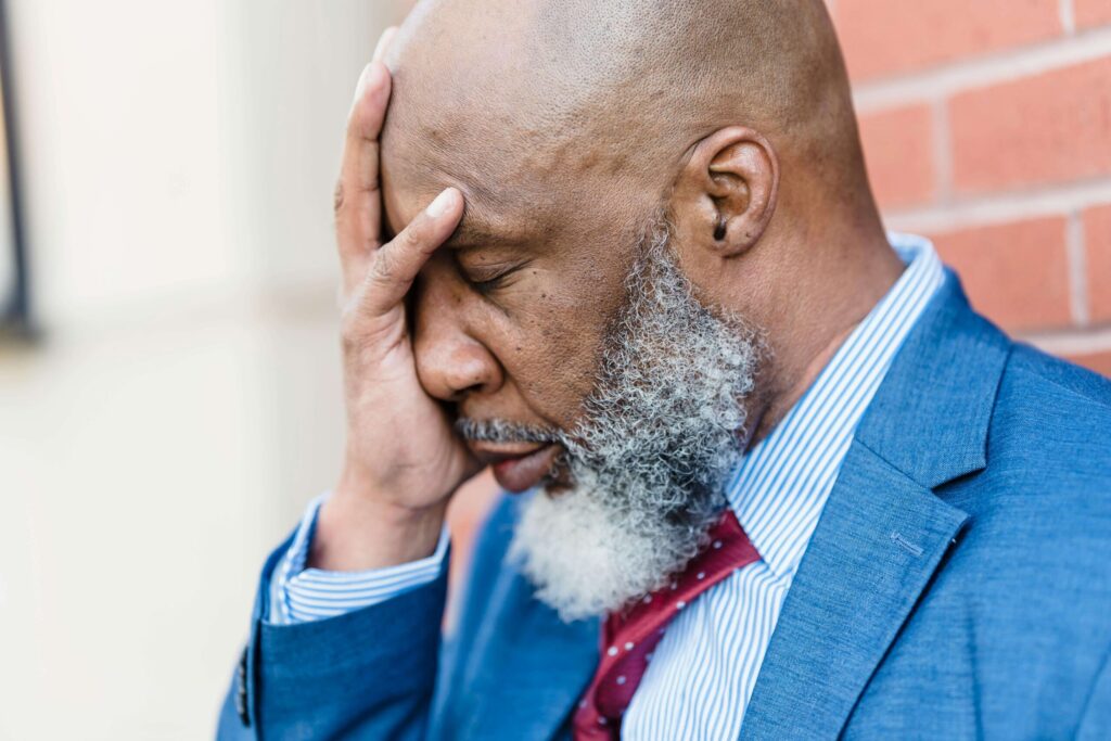 A professional Black man covering his face in distress wearing a suit. A therapist in Katy, TX can help with career stress, burnout & more. Reach out today to get started.