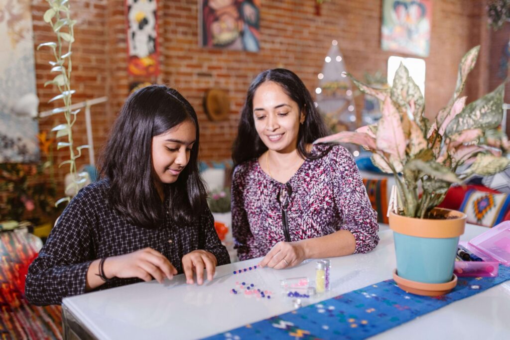 An older woman sitting with a child at a table arranging pink & blue beads. Child counseling for trauma in Katy, TX can support your family after a traumatic experience. Support your child today by calling us!