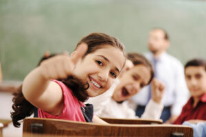 A little girl giving a thumbs up in a classroom setting. A child therapist in Katy, TX can support your child with anxiety, stress & behavioral problems. Get started with WHCC today!