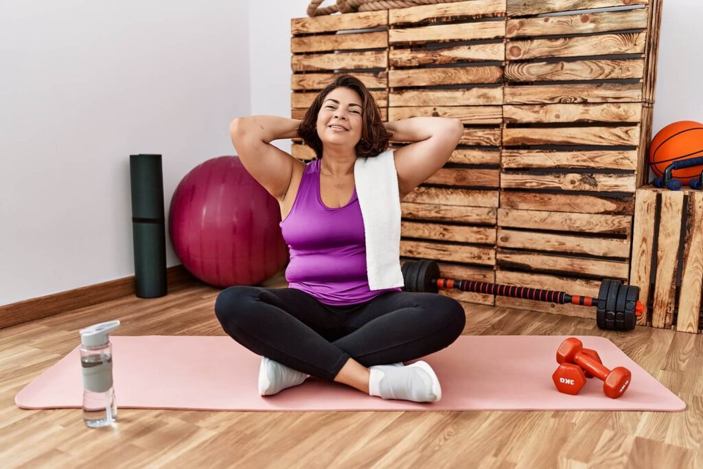 A woman sitting on a yoga mat with her hands resting behind her head. Representing how LENS therapy in Katy, TX can help you find relief. Reset your nervous system with a trusted therapist. 