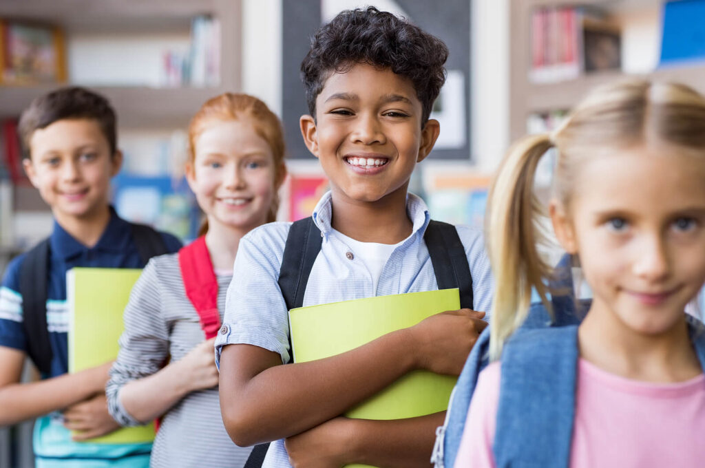 Diverse students smiling while lined up for class holding folders. Child behavioral therapy in Katy, TX can help with school anxiety, stress & unwanted behaviors. Get started today!