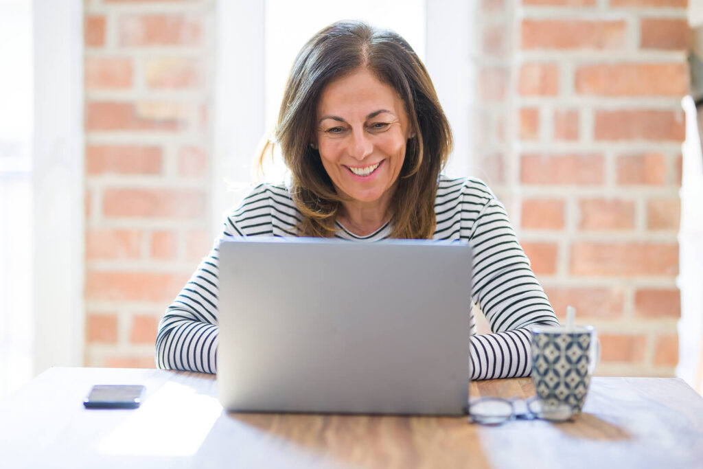 An older mature woman smiling at a laptop while sitting at a table with a coffee mug. Low-cost counseling in Katy, TX is here to support you. Reach out to our therapists to get started. 