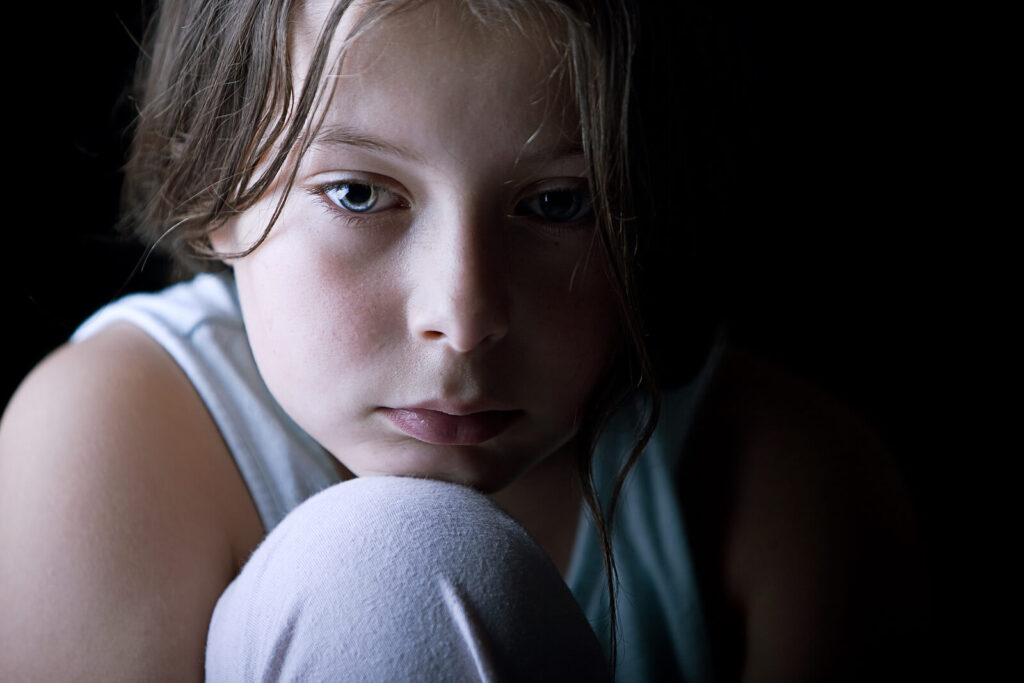An upset child resting their chin on their knee in a dark setting. Child behavioral therapy in Katy, TX is offered at different price points at WHCC. Contact us today to learn more. 