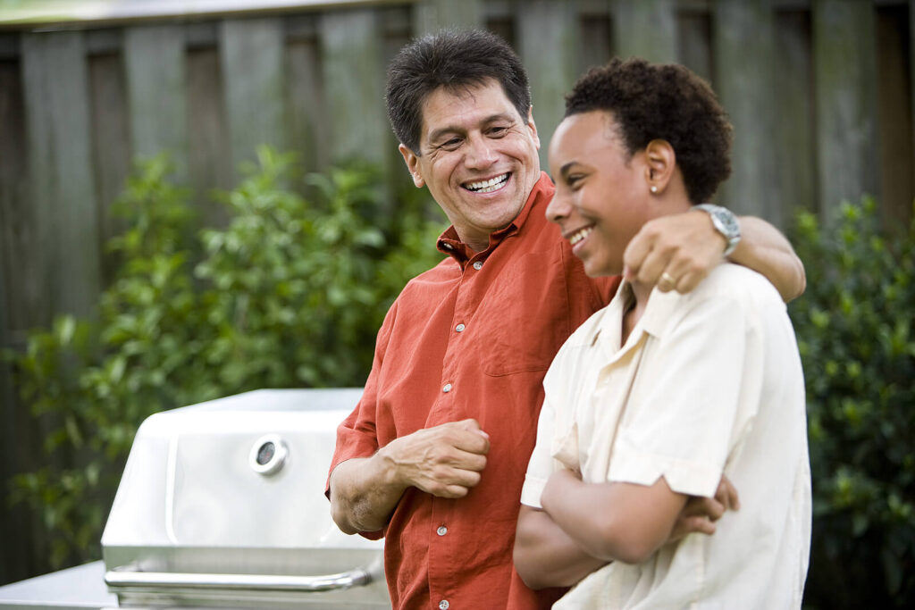 A happy father wrapping his arm around his son who is smiling outside near grill. Teen counseling in Katy, TX can help your teen thrive. Help your child today!