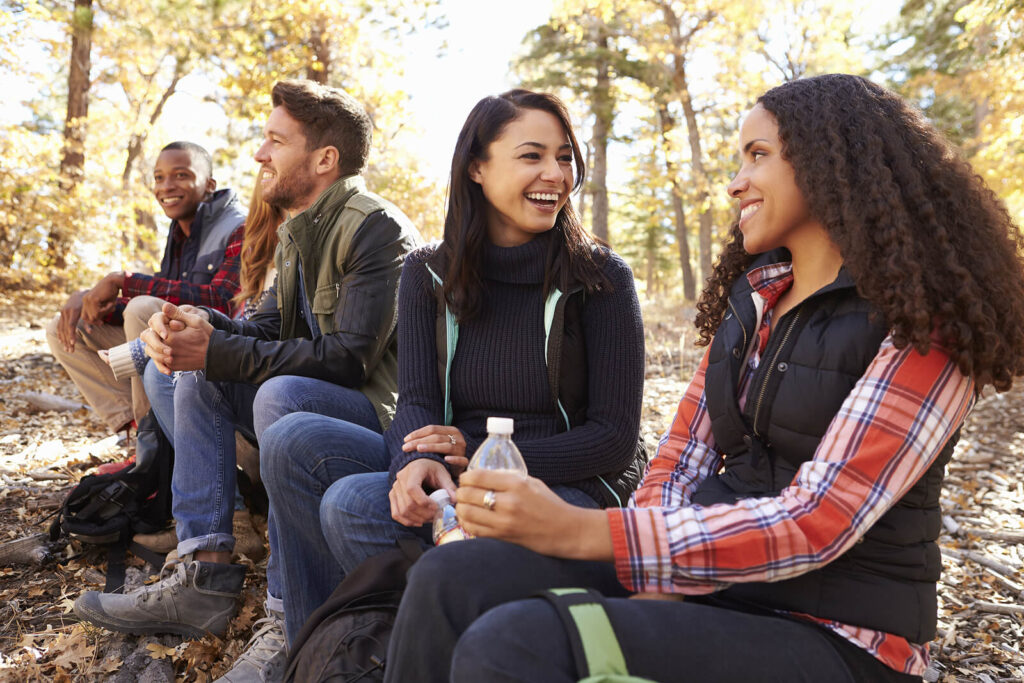 A group of biracial friend sitting outside in the woods all smiling. If you struggle with OCD or anxiety, we can help. Reach out to WHCC today for adult therapy in Katy, TX. 