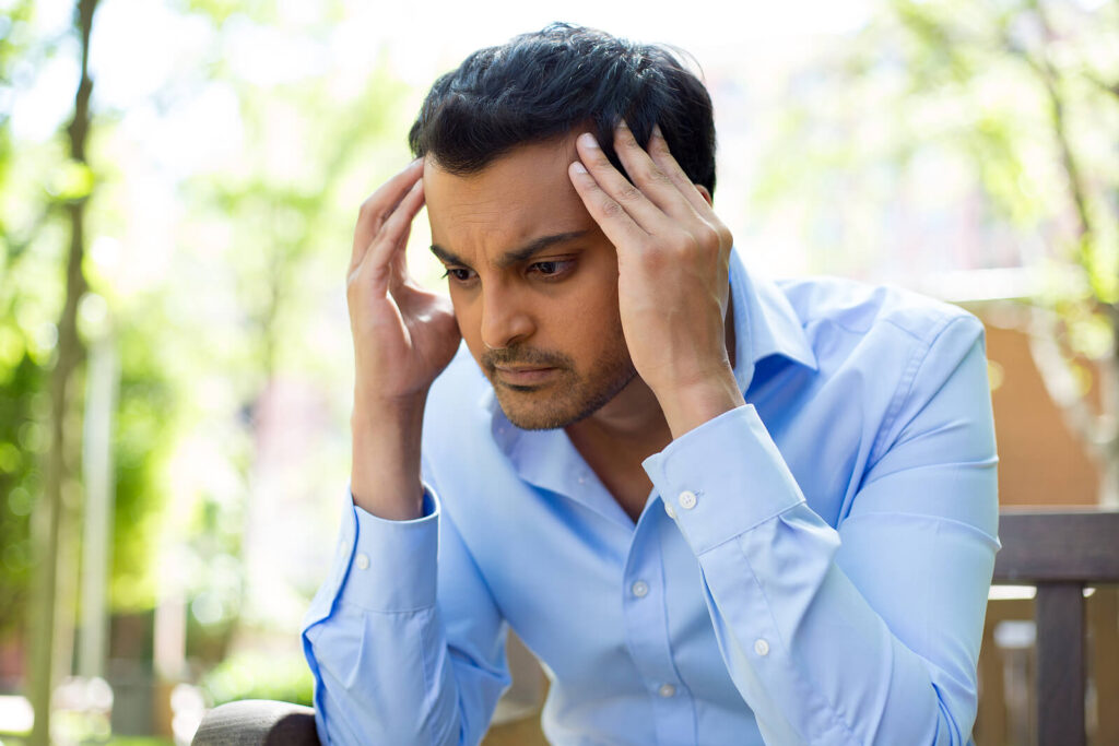 A professional man holding his head with anxious thoughts outside. Finding a therapist in Katy, TX can help you work through life transitions, work or parent struggles. Call today.