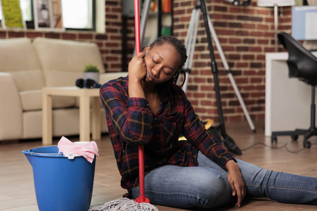An exhausted woman falling asleep while leaning on mop. Representing how the holidays can bring a ton of stress for moms & caregivers. Discover how women's counseling in Katy, TX can help with emotional exhaustion. 