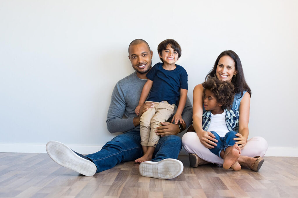 A happy diverse family sitting in front of a blank white wall, all smiling. Trauma counseling in katy, TX can help you heal from painful childhood memories. Get the support you deserve today.